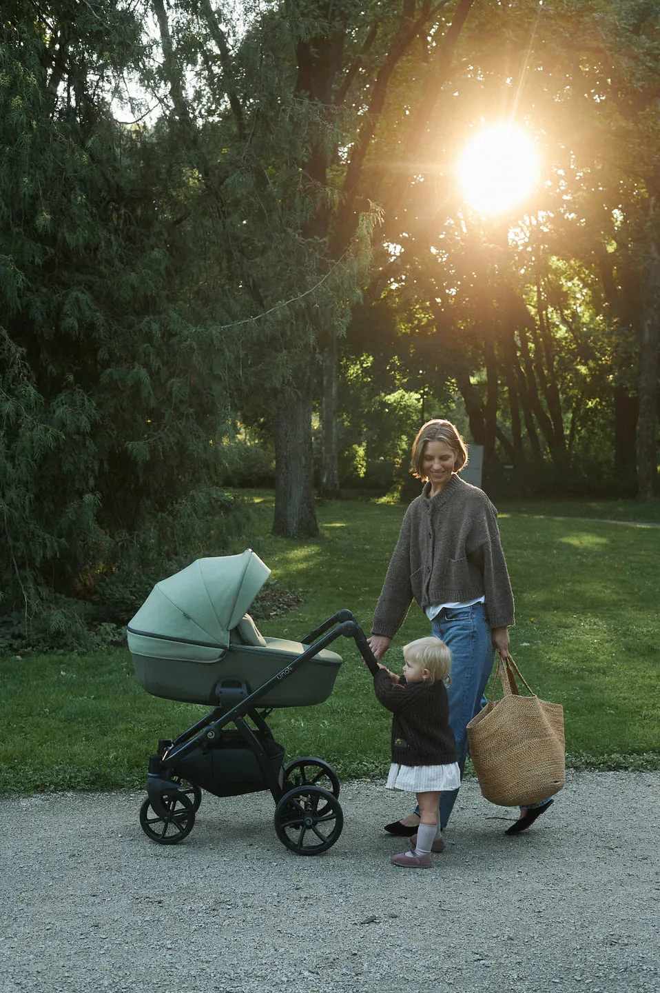 Mamma ar bērnu un Tutis Uno ratiņiem parkā saulrietā